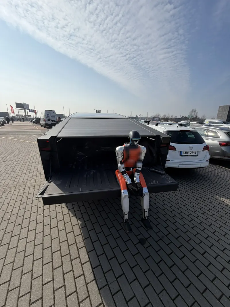 Humanoid sedí v otevřeném zavazadlovém prostoru vozu