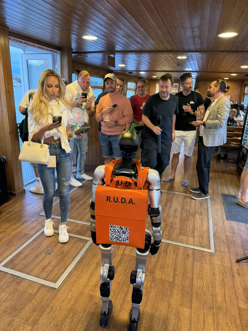 Humanoid v salonu lodi obklopený hosty