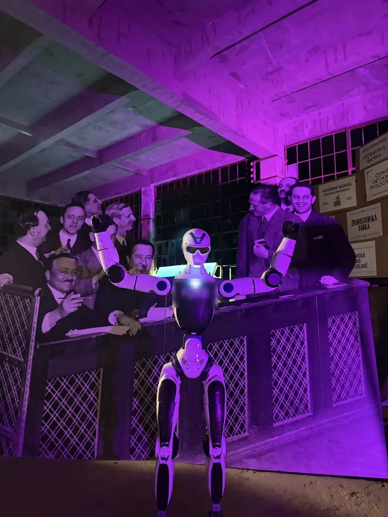 Humanoid tančí před DJ pultem obklopeným hosty